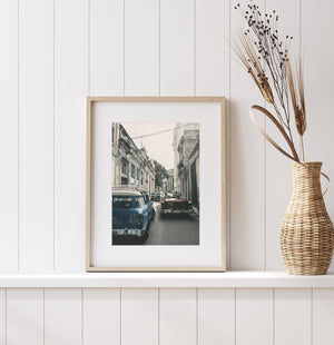 Vertical street photograph showing a blue vintage car, distant traffic and textured Havana architecture.