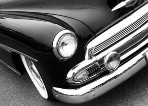 Polished chrome and a circular headlight define a vintage Chevrolet front corner in monochrome.