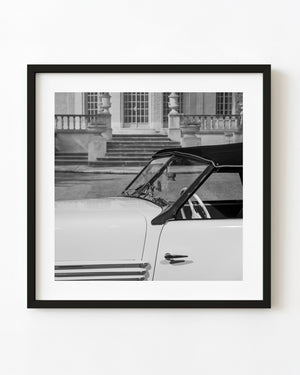 Black and white detail of a classic Cord roadster with a tilted windshield and smooth bodywork before a grand building.