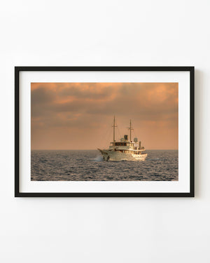 A classic white yacht sits on the Bahamas sea beneath warm evening clouds.