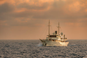 Colour nautical photograph of a vintage yacht on textured water under a peach-gold sky.