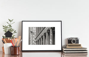 Horizontal black and white New York photograph of classical columns, ornate stonework and an American flag.