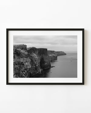 Black and white photograph of Ireland’s Cliffs of Moher receding above the Atlantic under a dark cloudy sky.
