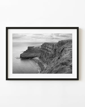 Black and white photograph of Ireland’s Cliffs of Moher above the Atlantic beneath an overcast sky.