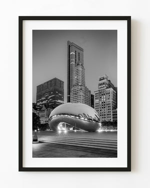 Black and white Chicago photograph of Cloud Gate reflecting the skyline beneath tall buildings in Millennium Park.