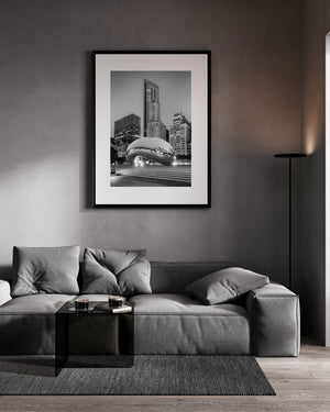 A tall Chicago tower rises behind the reflective Cloud Gate sculpture in monochrome.