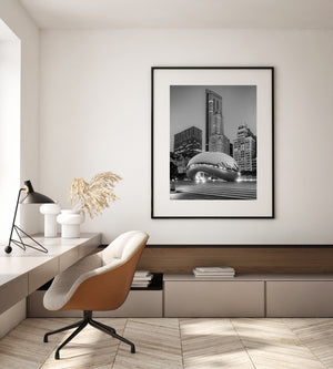 Reflections ripple across Cloud Gate below tall urban facades in a black and white Chicago photograph.