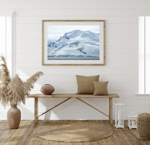 Horizontal Antarctic landscape photograph showing a cloud-wrapped snow mountain above coastal water.