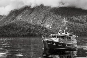 A dark-hulled vessel rests before mist-covered mountain slopes along the British Columbia coast.
