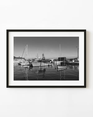 Black and white photograph of boats in Cobh Harbour with long mast reflections across calm water.