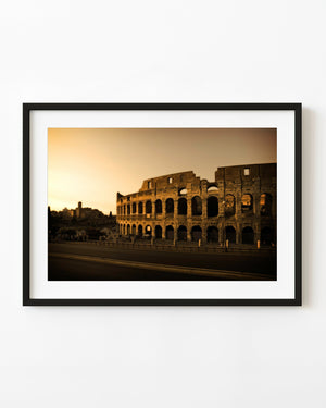 The Colosseum in Rome beneath a warm evening sky with deep shadows across its arches.