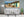 A panoramic Cuban street scene shows colourful homes, piled wood and distant mountain ridges.