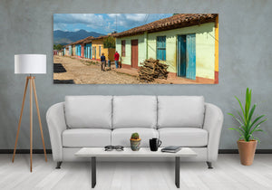 A panoramic Cuban street scene shows colourful homes, piled wood and distant mountain ridges.