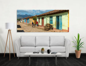 Sunlight falls across cobblestones beside a continuous row of painted houses in Trinidad.