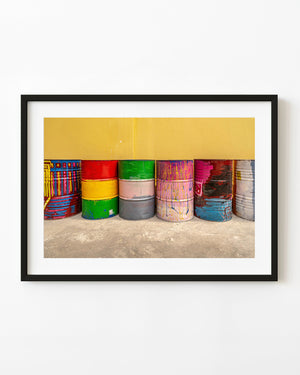 Colourfully painted barrels stand in a row beneath a yellow wall in Panama City.