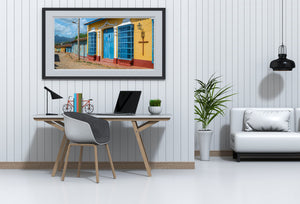 Tall blue metal grilles and decorative lamps punctuate a bright yellow house wall in Cuba.