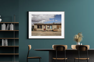 Horizontal desert architecture photograph showing an old gas station home under gathering clouds.