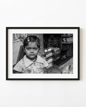 Black and white street portrait of a young girl beside a shop in Coonoor, India.