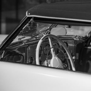 A white steering wheel stands against the dark dashboard of a classic Cord roadster.