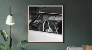 Monochrome vintage car detail showing the steering wheel, windscreen and polished interior fittings.