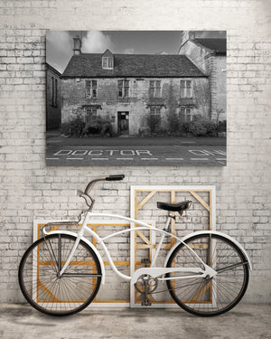 Horizontal black and white photograph of a historic Cotswolds building and its street setting.
