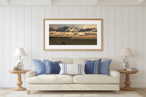 Wide coastal photograph of a couple sharing an ocean view beneath dramatic golden clouds.