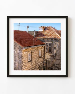 Weathered Croatian stone buildings and red tiled roofs stand beneath a clear blue sky.
