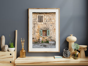 The rough stone facade of a Croatian house contrasts with bright turquoise window shutters.