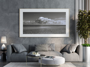 Ripples lead towards a distant horizon beneath billowing clouds in black and white.