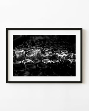 Rows of glass bottles catch bright rim highlights in a dark Cuban rum factory, photographed in black and white.