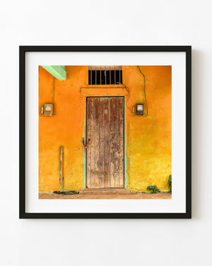 A weathered wooden door stands against a golden yellow wall in rural Cuba.