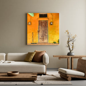 Looping wires and small electrical meters flank a wooden door on a sunlit yellow wall.