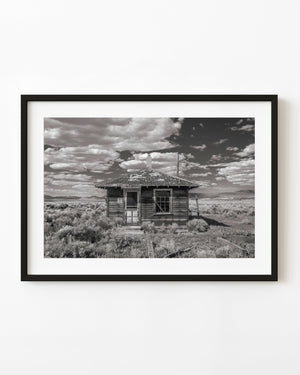 A weathered ghost town building stands among scrub beneath dramatic clouds in Currie Nevada.