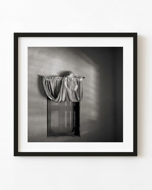 A loosely draped curtain hangs above a window in an abandoned Bahamas home, photographed in black and white.