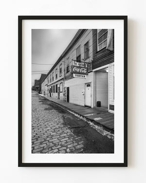 A cobblestone lane runs beside historic buildings at Custom House Wharf in Portland Maine, photographed in black and white.