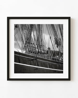 Dense ropes cross above the Cutty Sark’s weathered hull in a square black and white maritime photograph.