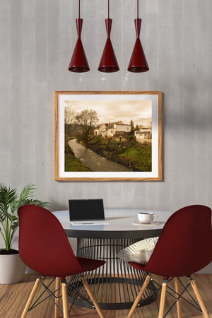 Cream walls and sloping roofs overlook a quiet Czech riverbank in soft golden light.