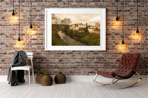 A quiet village landscape combines pale houses, grassy riverbanks and leafless trees.