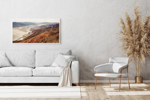 Rough foreground slopes frame a broad view of pale desert flats and hazy mountain ranges.