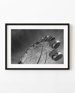 Darling Harbour’s Ferris wheel rises diagonally against dark clouds in black and white.