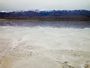 Cracked white salt patterns lead toward a reflected mountain range in Badwater Basin.
