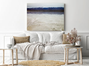 Blue-grey mountain slopes and bright snow rise above a narrow reflective strip of water.