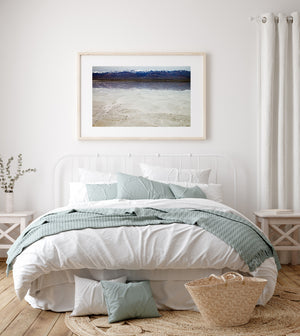 A snowy mountain outline repeats softly in shallow water beside Death Valley’s salt flats.