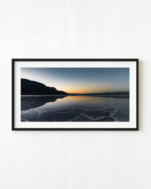 An orange twilight horizon reflects across cool blue salt flats beneath dark mountains in Death Valley.