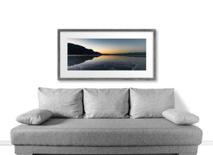Dark mountain silhouettes surround calm water reflecting the last warm light of evening.