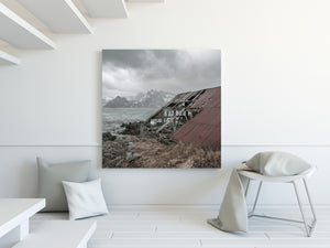 Snow-marked mountains rise across the sea beyond a damaged wooden boathouse in Norway.