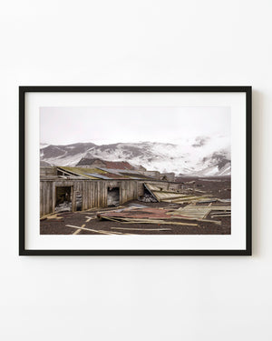 Weathered wooden ruins lie below a broad snowy ridge at Whalers Bay on Deception Island, Antarctica.