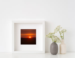 Orange light near the sun fades into darker red sky above a quiet rural landscape.