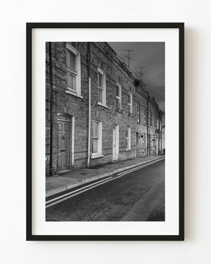 Derry brick terrace beside an empty street at dusk, black and white photograph.