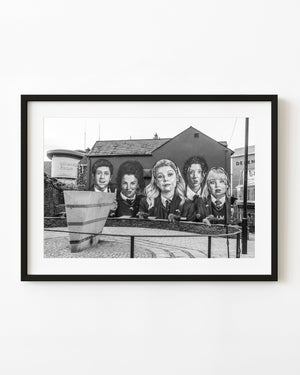 Derry Girls mural above curved paving and railings, black and white street photograph.